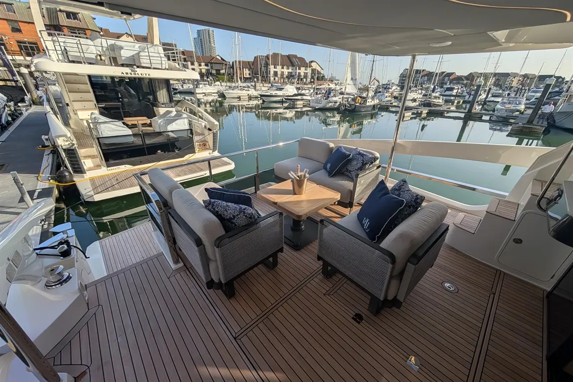 Luxury yacht deck with seating, a table, and an ice bucket, overlooking a marina filled with boats and calm water.